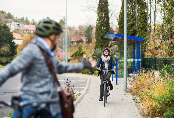 An active senior couple with helmets and electrobikes cycling outdoors on a pathway in town.