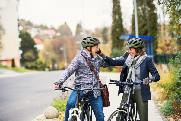 Happy active senior people with electrobikes greeting outdoors on a road in town.