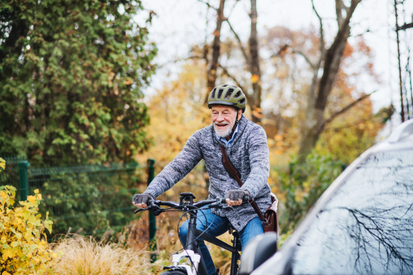 An active senior man with helmet and electrobike cycling outdoors in autumn in park.