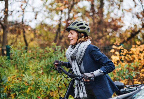 An active senior woman with helmet and electrobike cycling outdoors in autumn in park.