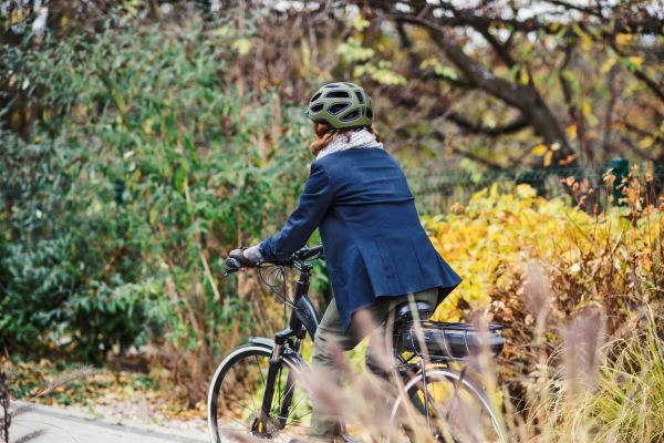 A rear view of unrecognizable active senior woman with electrobike cycling outdoors in park.