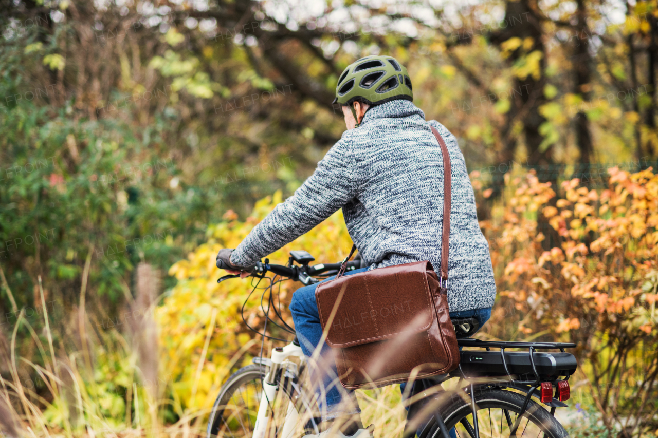 An active senior man with helmet and electrobike cycling outdoors in autumn in park.