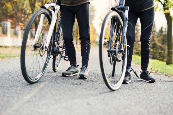 Legs and feet of couple with electrobikes outdoors on a road in park. Copy space.