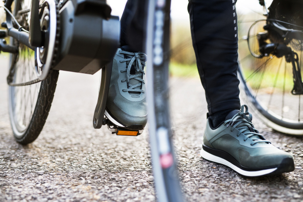 A close-up of legs and feet on pedal of electrobike outdoors on a road in park.