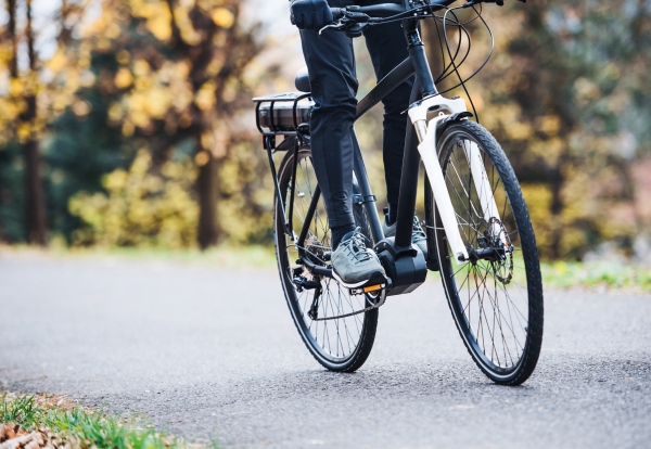 An unrecognizable man on an electrobike cycling outdoors on a road in park.