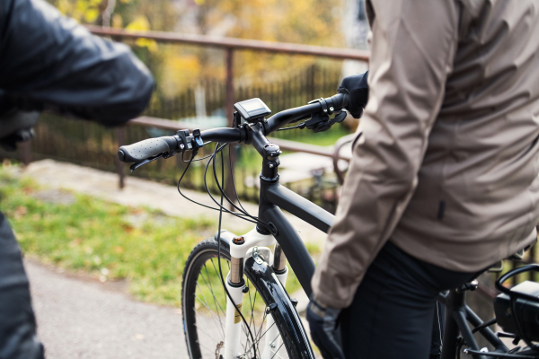 A midsection of active senior couple with helmets and electrobikes cycling outdoors on a road.