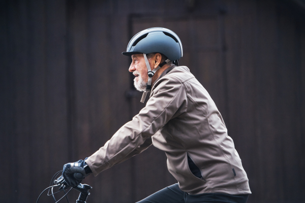 A side view of an active senior man with bike helmet cycling outdoors against dark background.