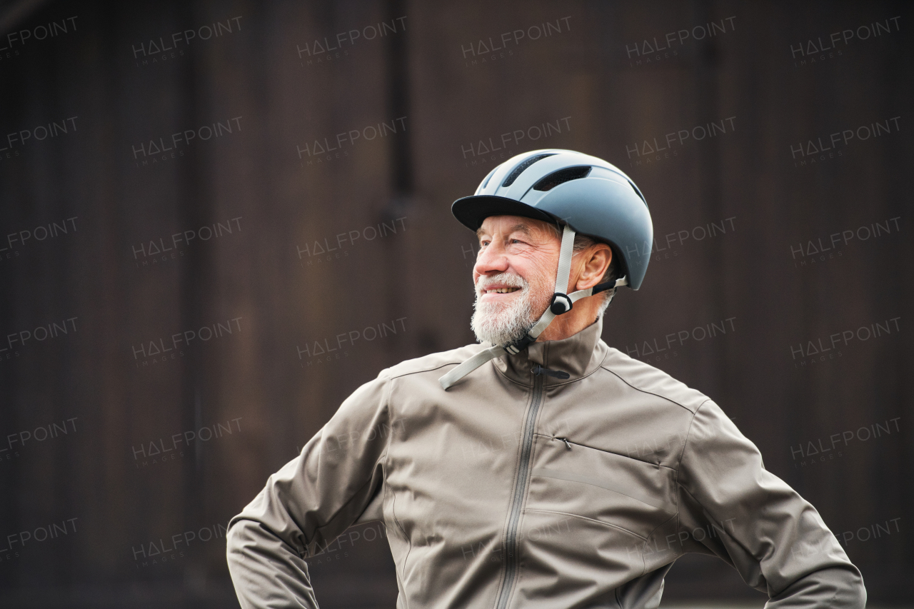 Cheerful active senior man with bike helmet standing outdoors against dark background.