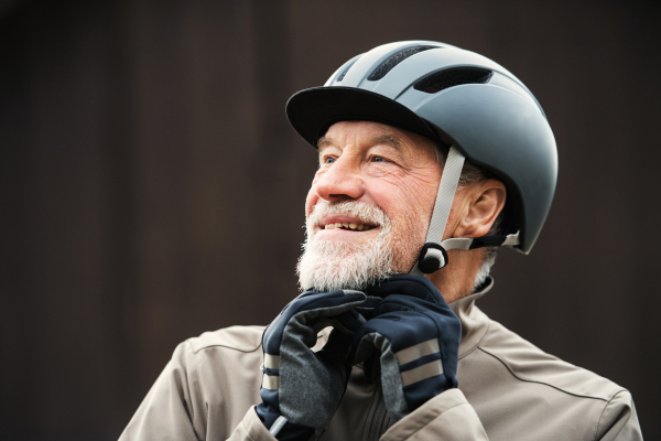 An active cheerful senior man standing outdoors in town, putting on a bike helmet.