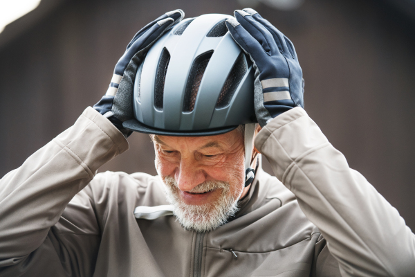 An active cheerful senior man standing outdoors in town, putting on a bike helmet.