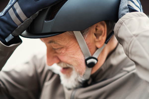 A close-up of active cheerful senior man standing outdoors in town, putting on a bike helmet.