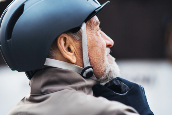 A close-up of active senior man standing outdoors in town, putting on a bike helmet.