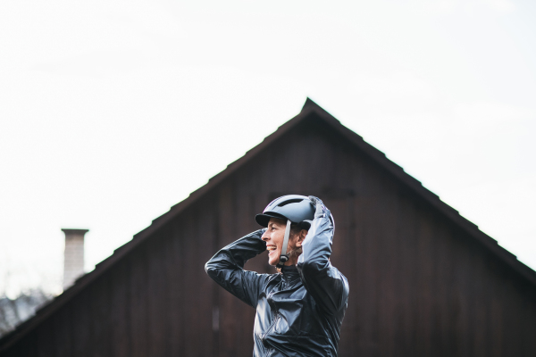 A cheerful active senior woman standing outdoors, putting on bicycle helmet. Copy space.