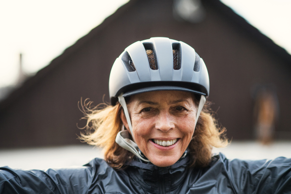 A front view portrait of cheerful active senior woman standing outdoors in front of a house.