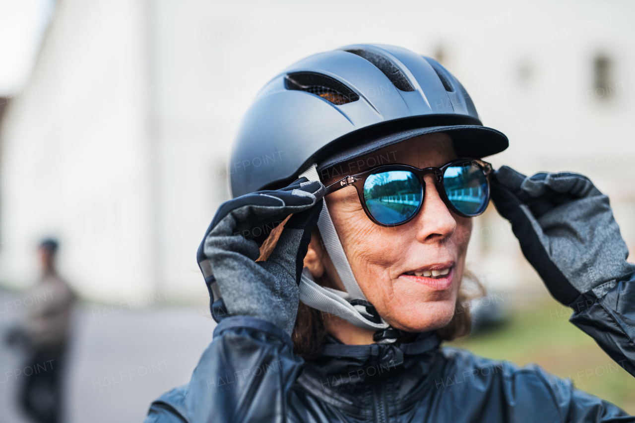 Close-up of active senior woman with bike helmet standing outdoors, putting on sunglasses.