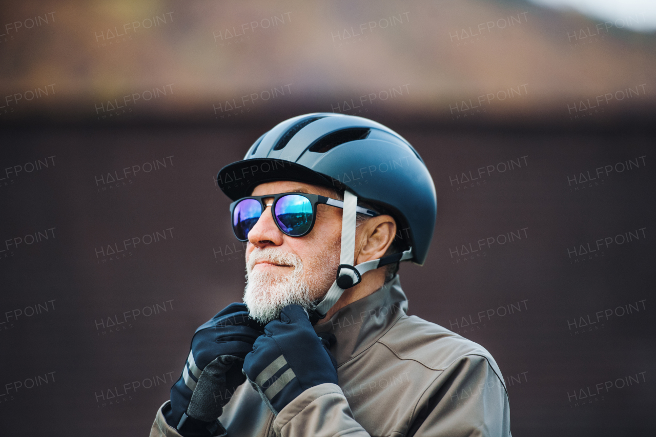 An active senior man with sunglasses standing outdoors in town, putting on a bike helmet.