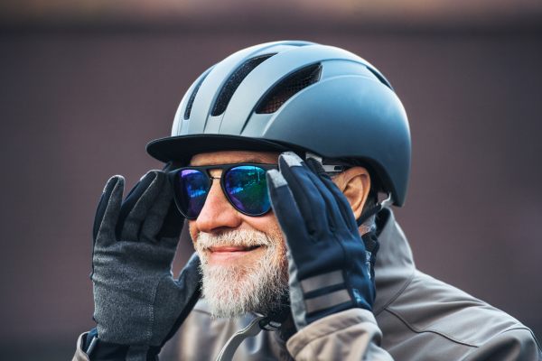 A close-up of active senior man standing outdoors, putting on sunglasses.