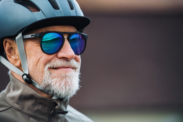 Close-up of active senior man with sunglasses and bicycle helmet standing outdoors. Copy space.