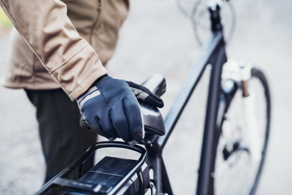 A midsection of an unrecognizable cyclist with electrobike standing outdoors in town.