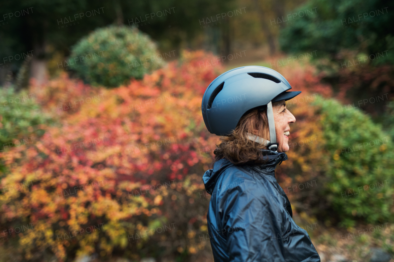 A side view of active senior woman with bicycle helmet standing outdoors in nature. Copy space.