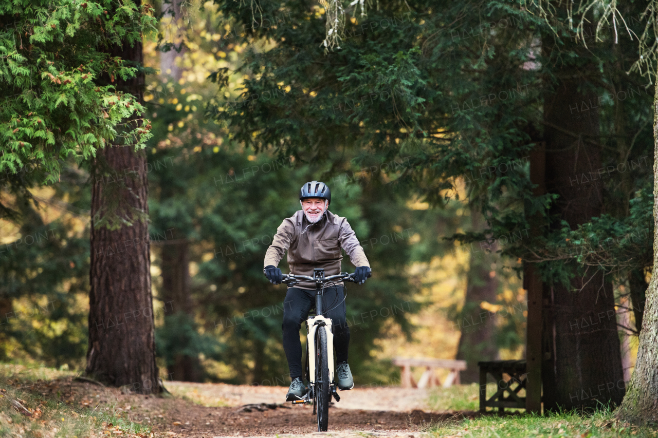 An active senior man with electrobike cycling outdoors on a road in park in autumn. Copy space.