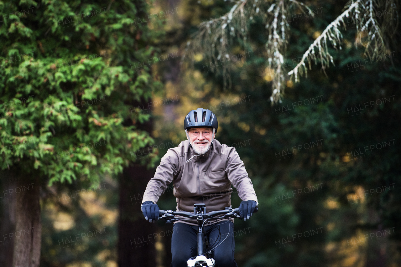 An active senior man with helmet and electrobike cycling outdoors on a road in nature.