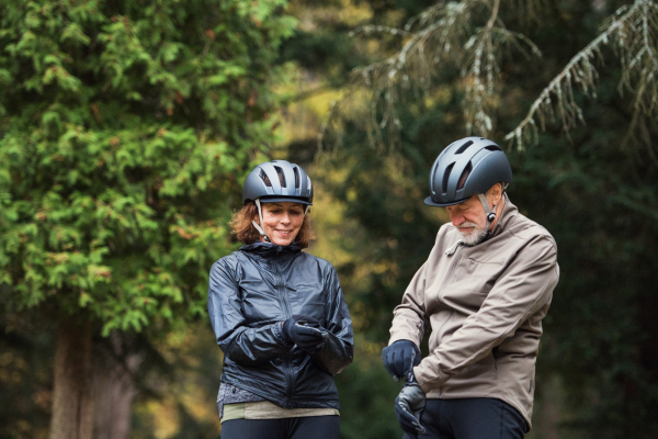 A happy senior couple with bicycle helmet standing outdoors on a road in park in autumn.