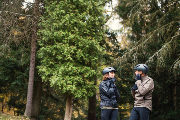 A happy senior couple with bicycle helmet standing outdoors on a road in park in autumn.