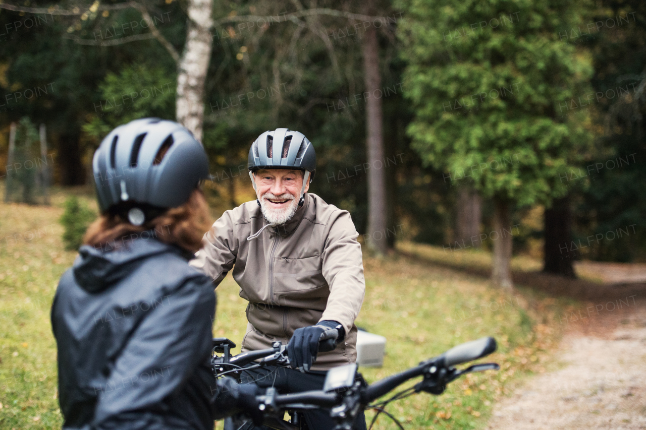 A happy senior couple with bicycle helmet standing outdoors on a road in park in autumn.