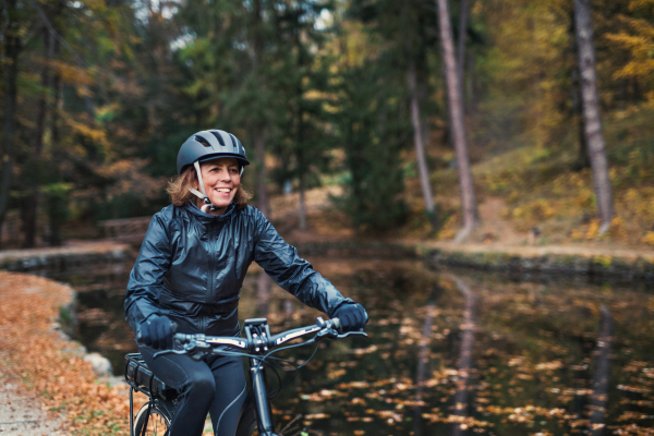 An active senior woman with electrobike cycling outdoors on a road in park in autumn. Copy space.