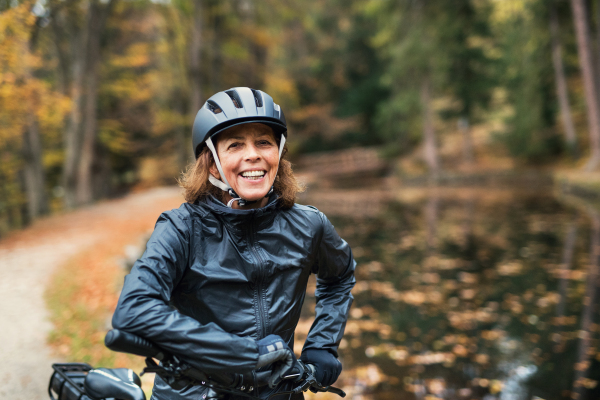 An active senior woman with electrobike standing outdoors on a road in park in autumn. Copy space.