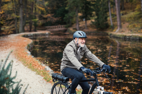 An active senior man with electrobike cycling outdoors on a road in park in autumn. Copy space.