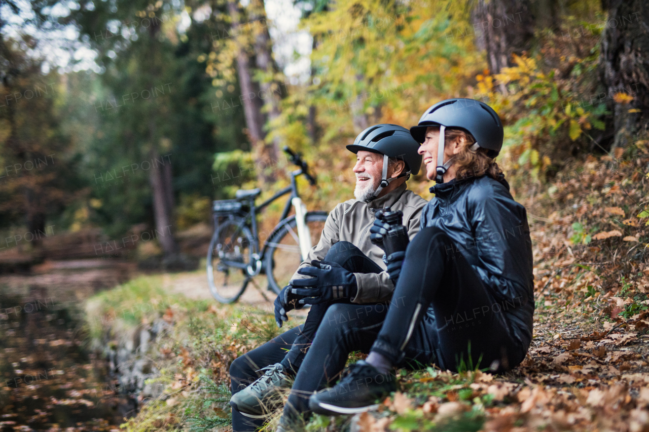 A senior couple with electrobikes sitting outdoors in park in autumn nature, resting.