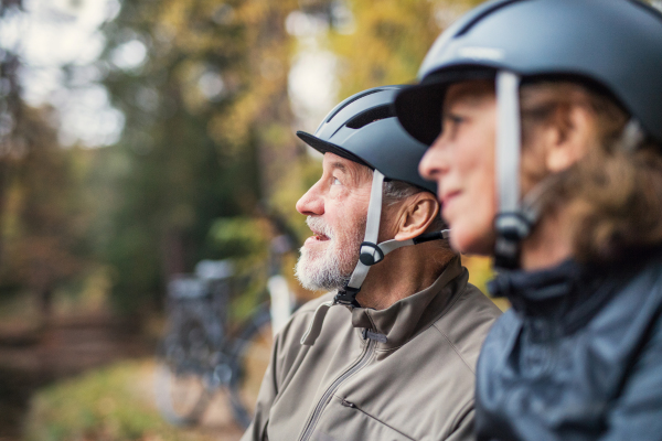 A happy senior couple with bicycle helmet standing outdoors in park in autumn.