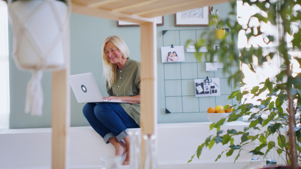 Attractive senior woman sitting indoors at home, using laptop when resting.