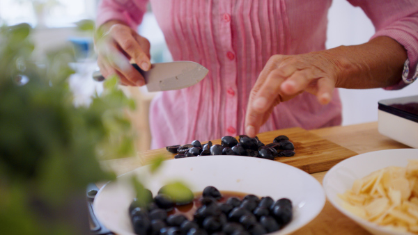 Midsection of unrecognizable woman cooking in kitchen indoors, chopping olives.