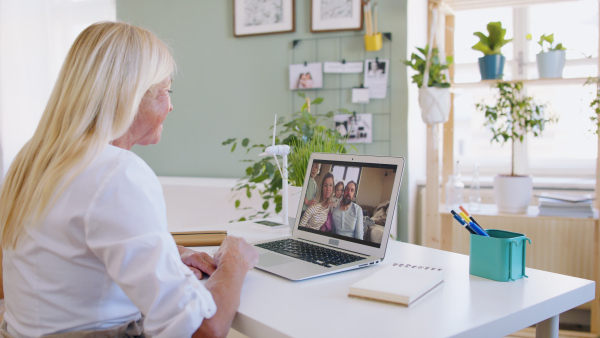 Happy senior woman with laptop indoors at home, family video call concept.