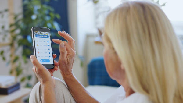 Unrecognizable woman with smartphone indoors at home, ordering food online.