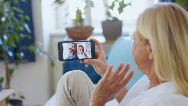 Happy senior mother talking to son and grandchidlren indoors at home, family video call concept.