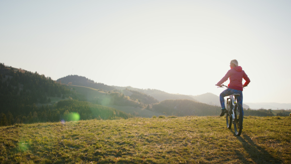 Rear view of active senior woman with e-bike cycling outdoors in nature.