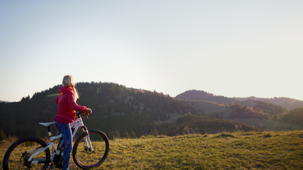 Side view of active senior woman with e-bike cycling outdoors in nature.