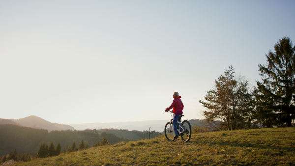 Rear view of active senior woman with e-bike cycling outdoors in nature.