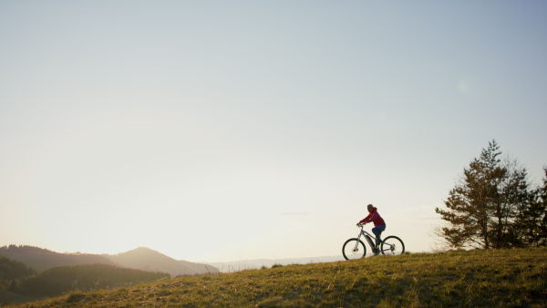 Side view of active senior woman with e-bike cycling outdoors in nature.