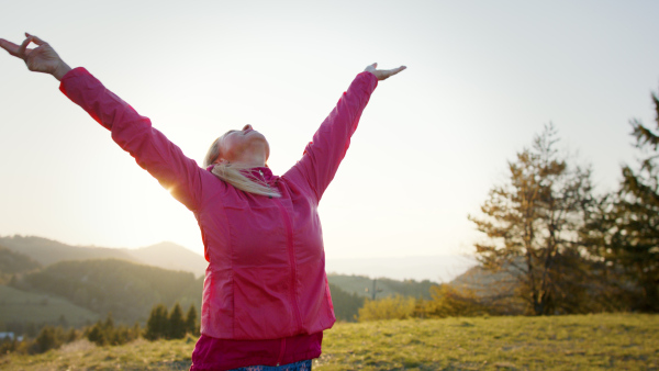 Attractive senior woman stretching arms outdoors in nature, meditating.