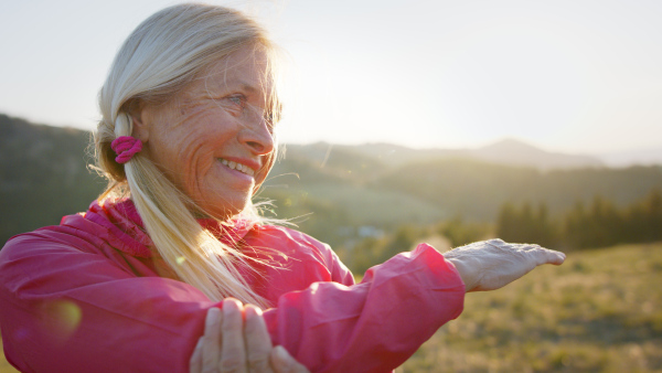 Happy attractive senior woman doing exercise outdoors in nature, stretching.