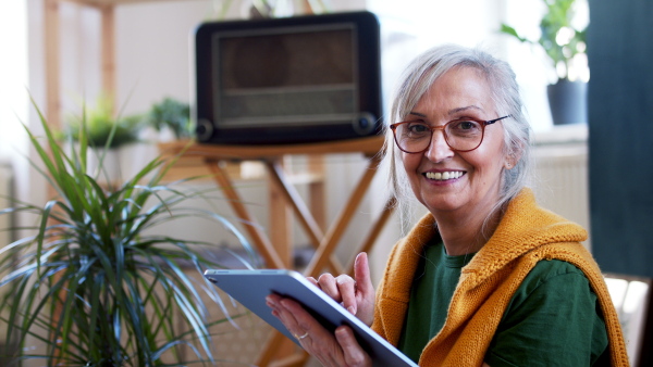 Portrait of senior woman designer with tablet sitting on floor at home, working.