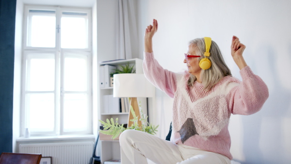 Portrait of cheerful senior woman with sunglasses and headphones indoors at home, laughing.