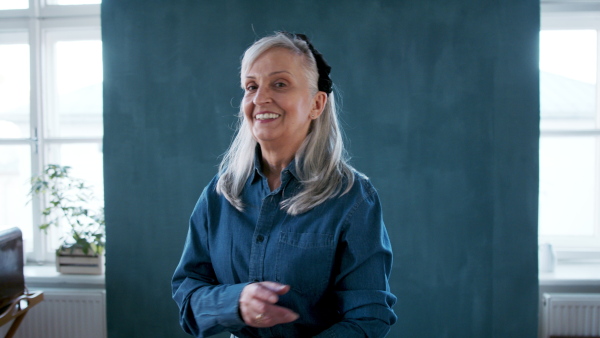 Front view portrait of senior woman standing indoors against dark background, looking at camera.