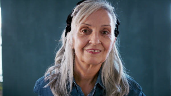 Front view portrait of senior woman standing indoors against dark background, looking at camera.