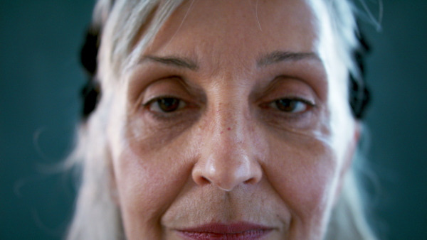 Front view close up of senior woman standing indoors against dark background, looking at camera.